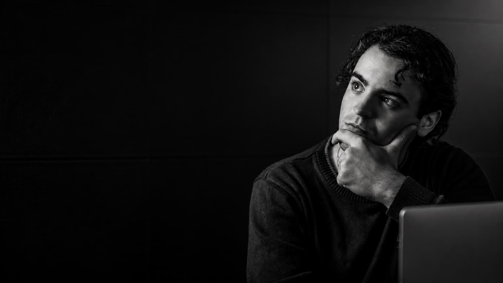 Vinicius Brigido em retrato editorial, sentado diante de um notebook e olhando para a esquerda.